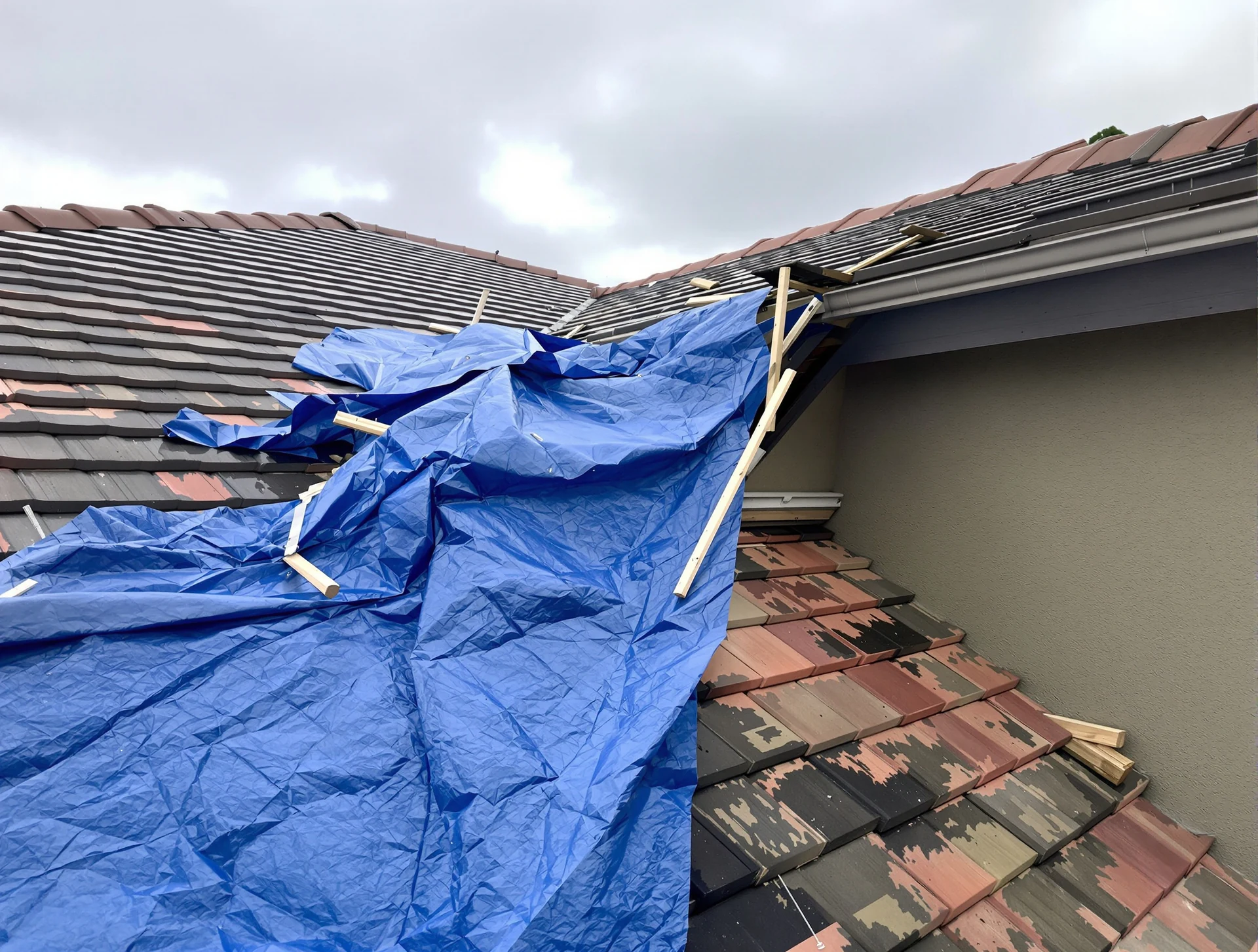 Emergency tarp fastened over storm damage on a tile roof