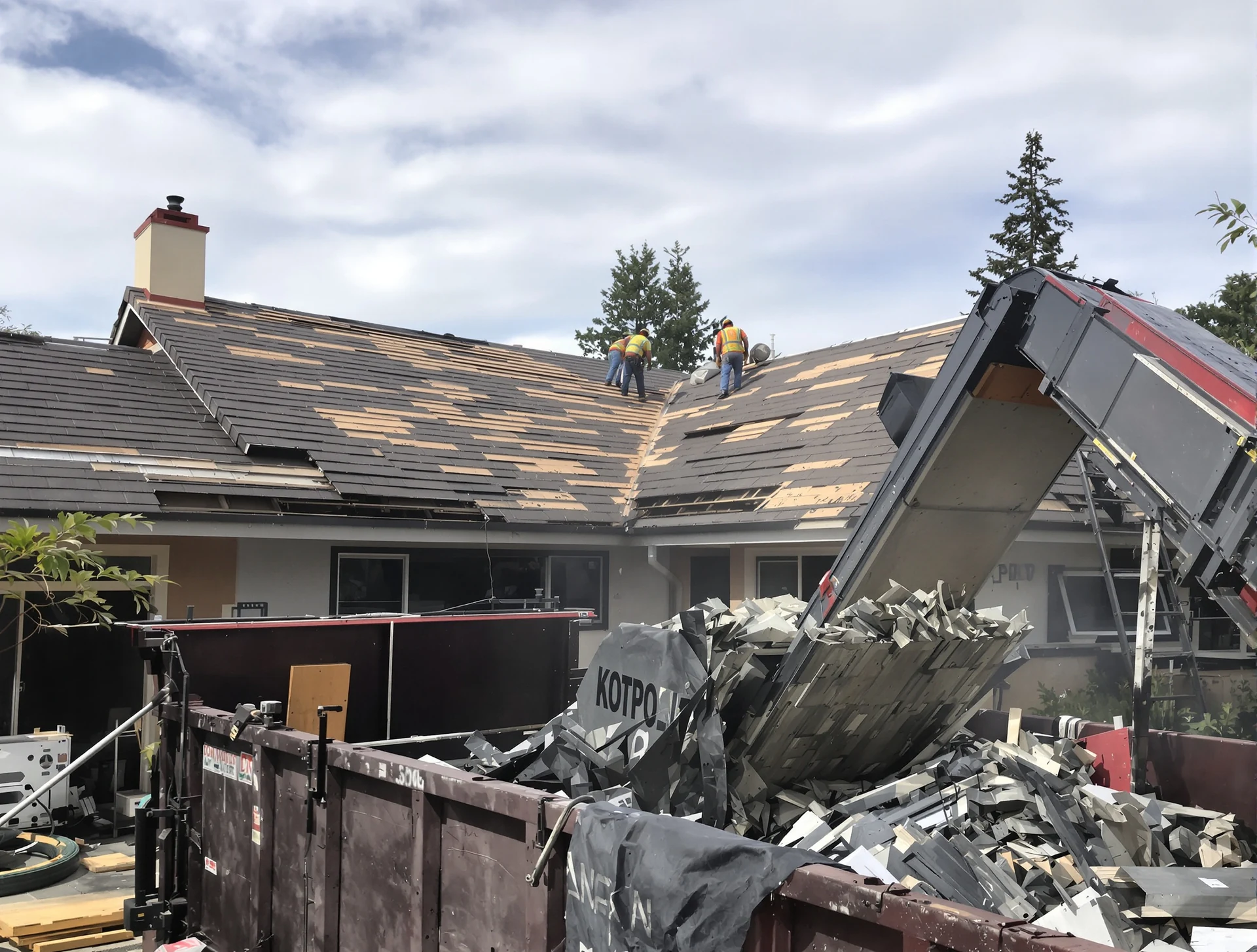 Old roof being torn off into a bin in the driveway